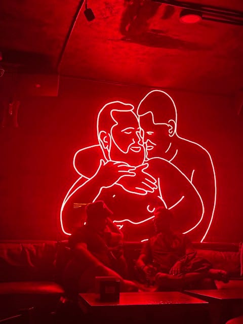 Two queers coverse under the neon lit bears at STUDS bar. A refreshing pool overlooks Playa de Los Muertos and the sprawl of blue umbrellas at Mantamar beach club in Puerto Vallarta, Mexico.