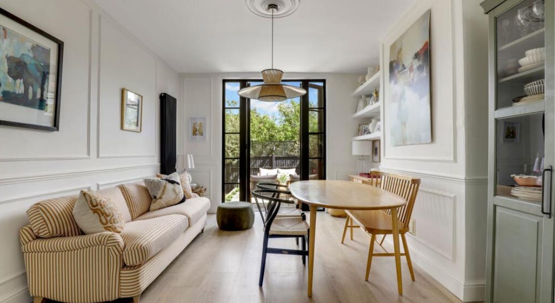 A dining area with a yellow striped sofa, a wooden table, white walls, and a mint green bookcase