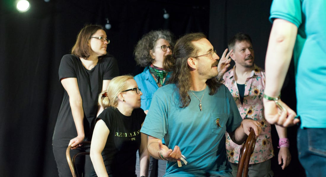 A group of people wearing blue and black t-shirts standing on a stage looking to the right