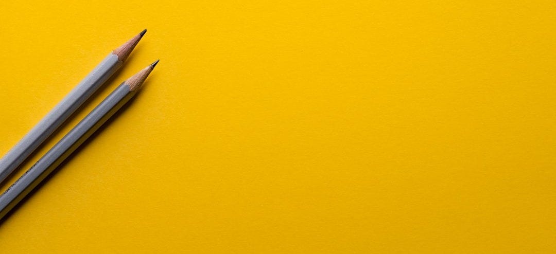 two gray pencils on yellow surface