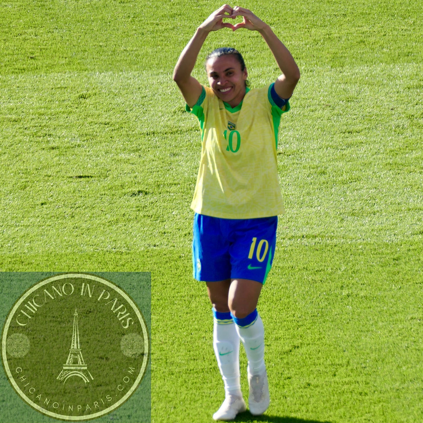 Soccer player, Marta, in Brazil's yellow and blue national team jersey with number 10, standing on a grass field and making a heart shape with both hands raised above their head in celebration