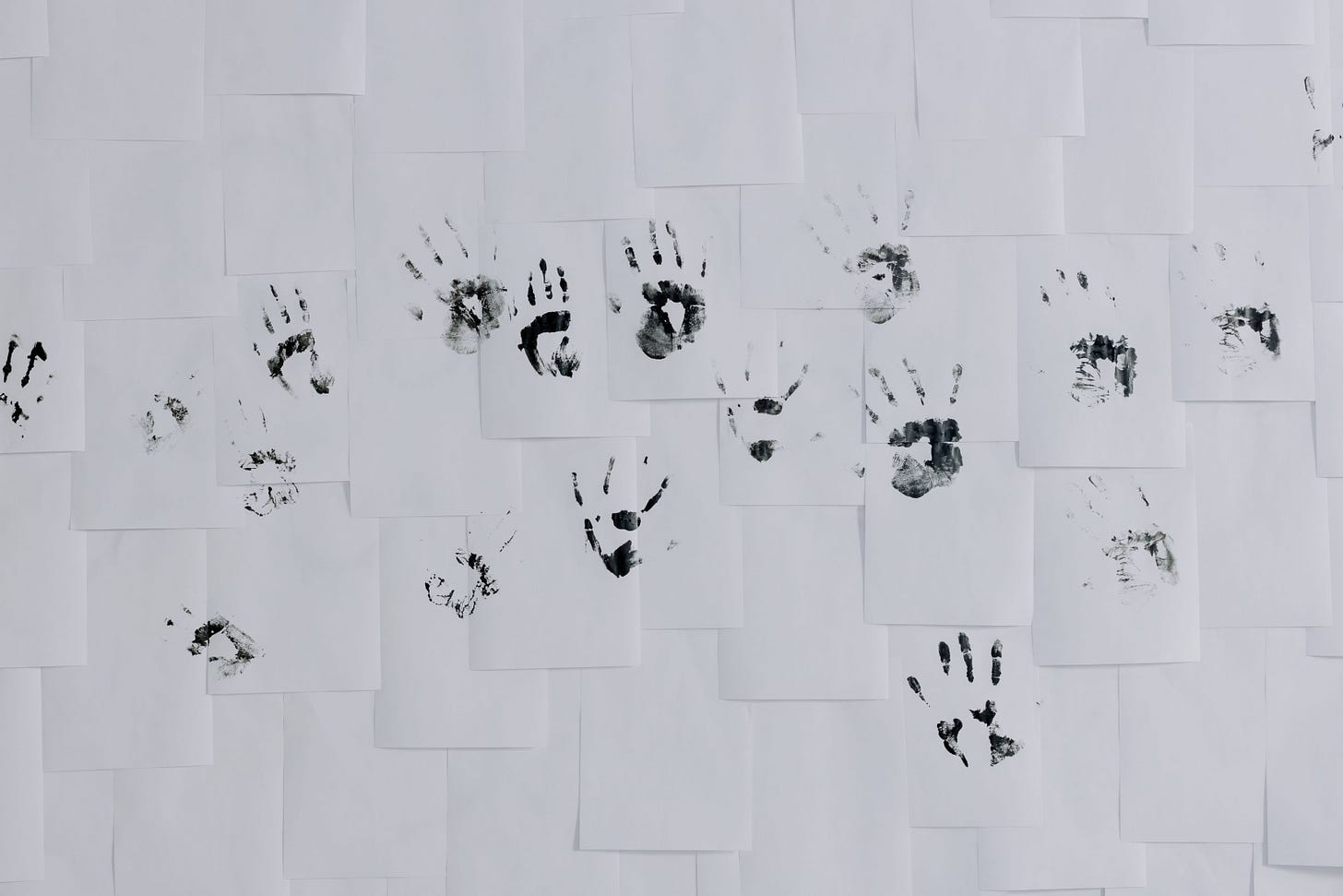 Black ink handprints scattered across overlapping white sheets of paper, the article's image for many hands on one record.