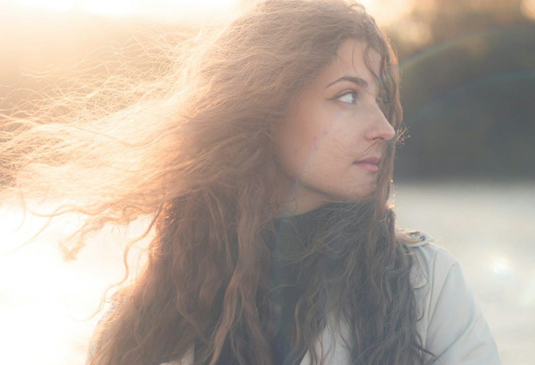 a woman standing on a beach with her hair blowing in the wind