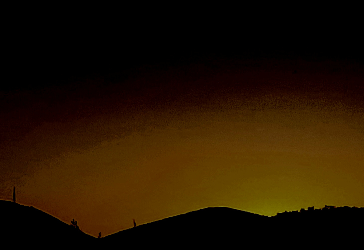 Black sky turning to orange and then yellow as sun peeks from behind mountain