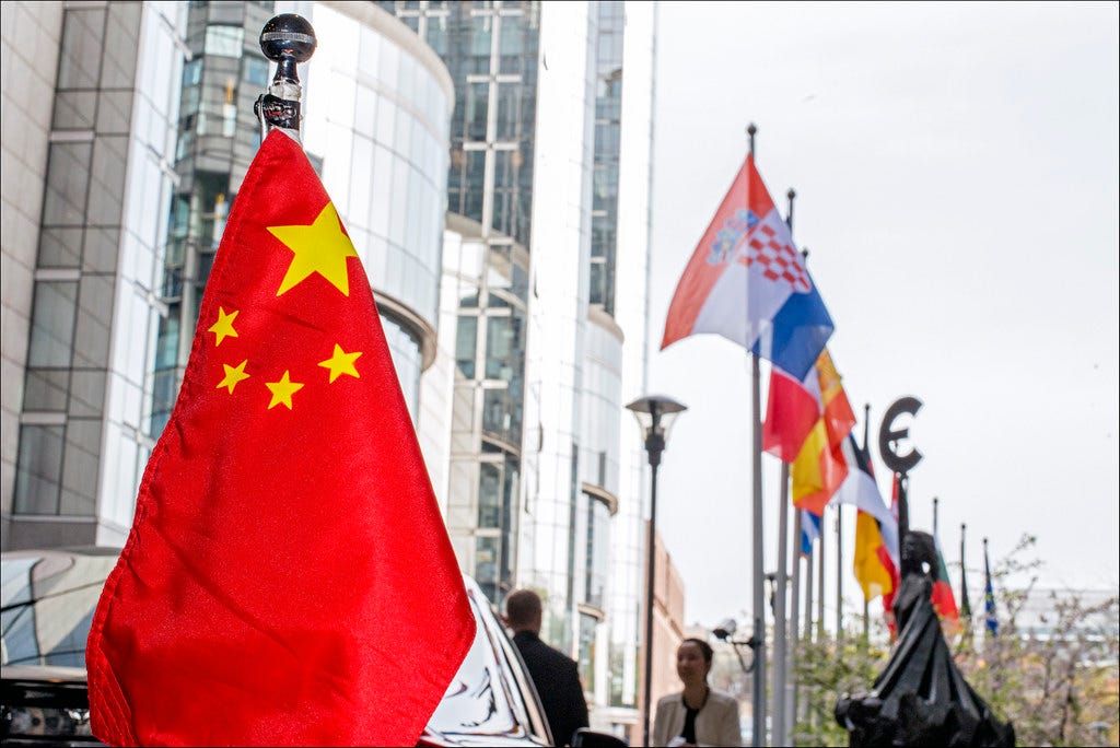 Foto de bandeiras no prédio do Parlamento Europeu, com a bandeira da China em primeiro plano e outras bandeiras europeias e o logo do Euro Foto de bandeiras no prédio do Parlamento Europeu, com a bandeira da China em primeiro plano e outras bandeiras europeias e o logo do Euro