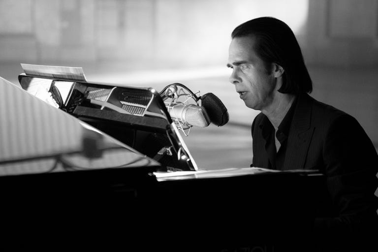 Nick Cave sings while sitting at a piano. Nick Cave sings while sitting at a piano.
