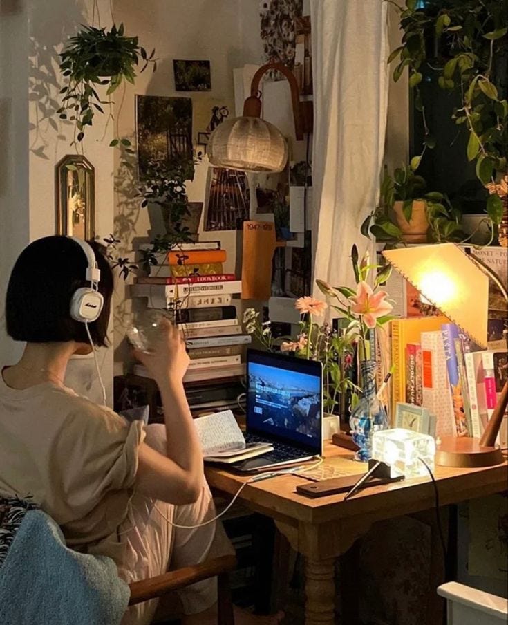 This may contain: a woman sitting at a desk with headphones on and looking at a computer screen