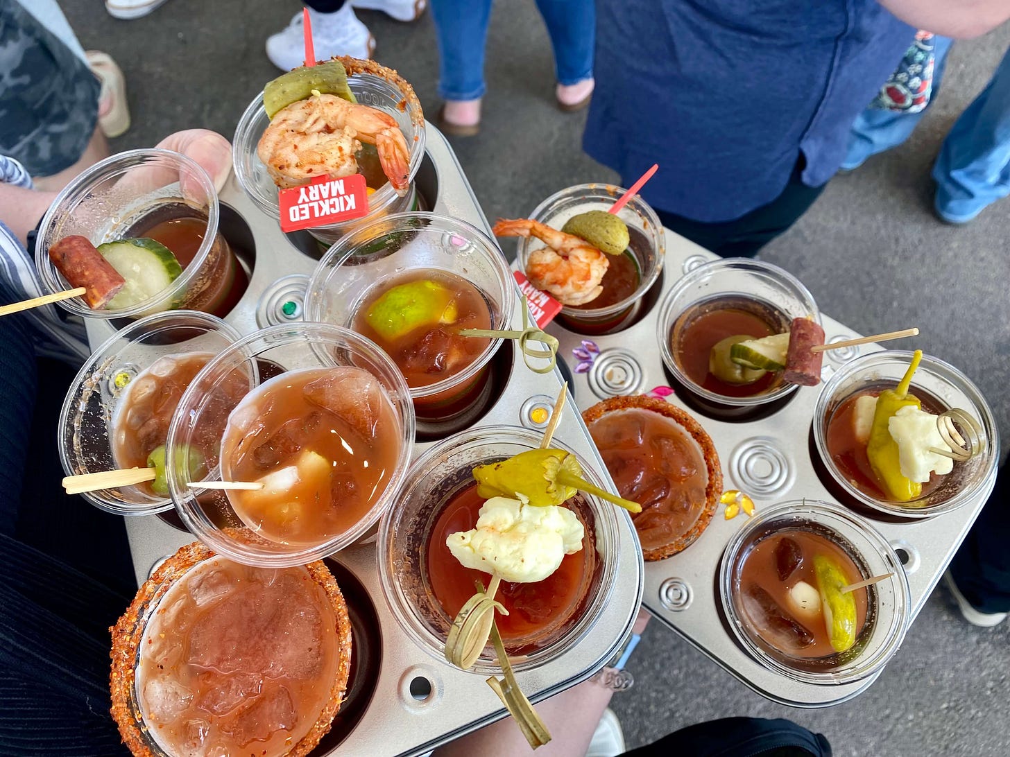 Two cupcake trays filled with mini cups of Bloody Mary.