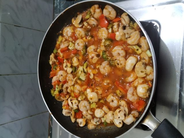 A black pan with prawns, brocoli, mushrooms in tomato sauce