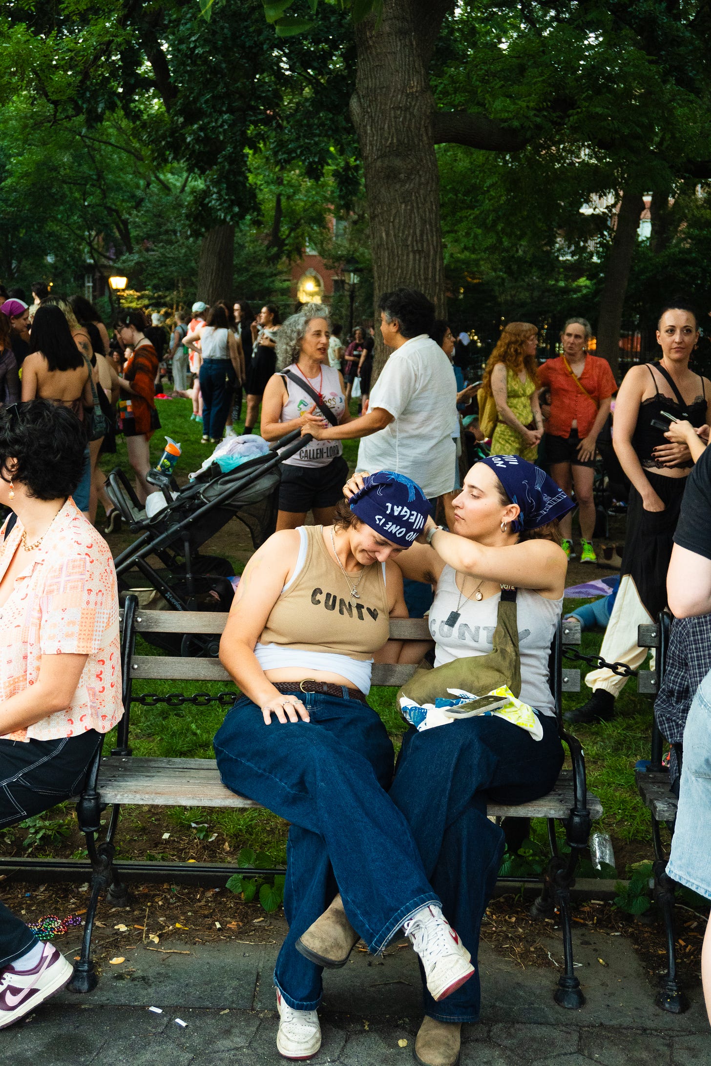 A couple on a bench in washington square park. One is fixing the bandana of the other with the utmost focus and care. 