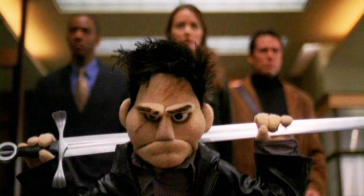 The puppet angel holding a sword over his back with his friends blurred in the background
