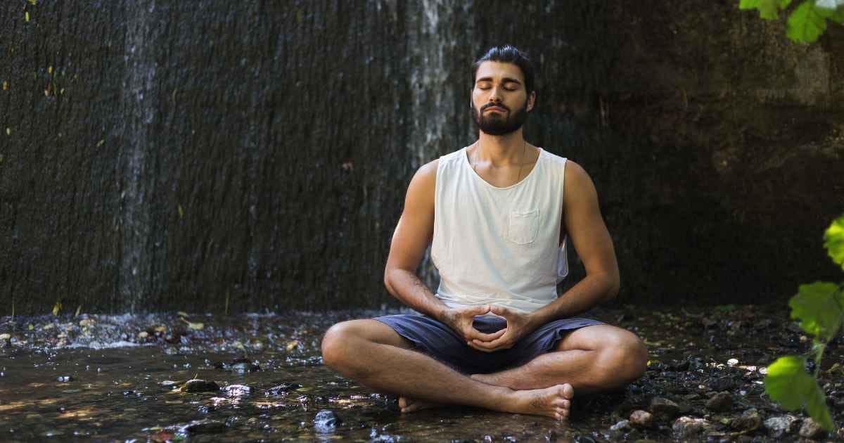 man meditating near waterfall