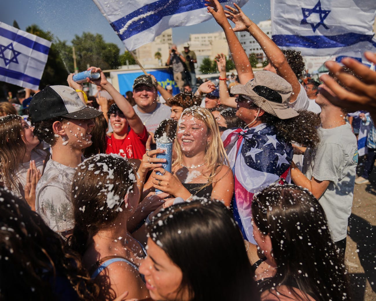 People wave Israeli flags and spray foam in celebration after the arrival of freed hostages. People wave Israeli flags and spray foam in celebration after the arrival of freed hostages.