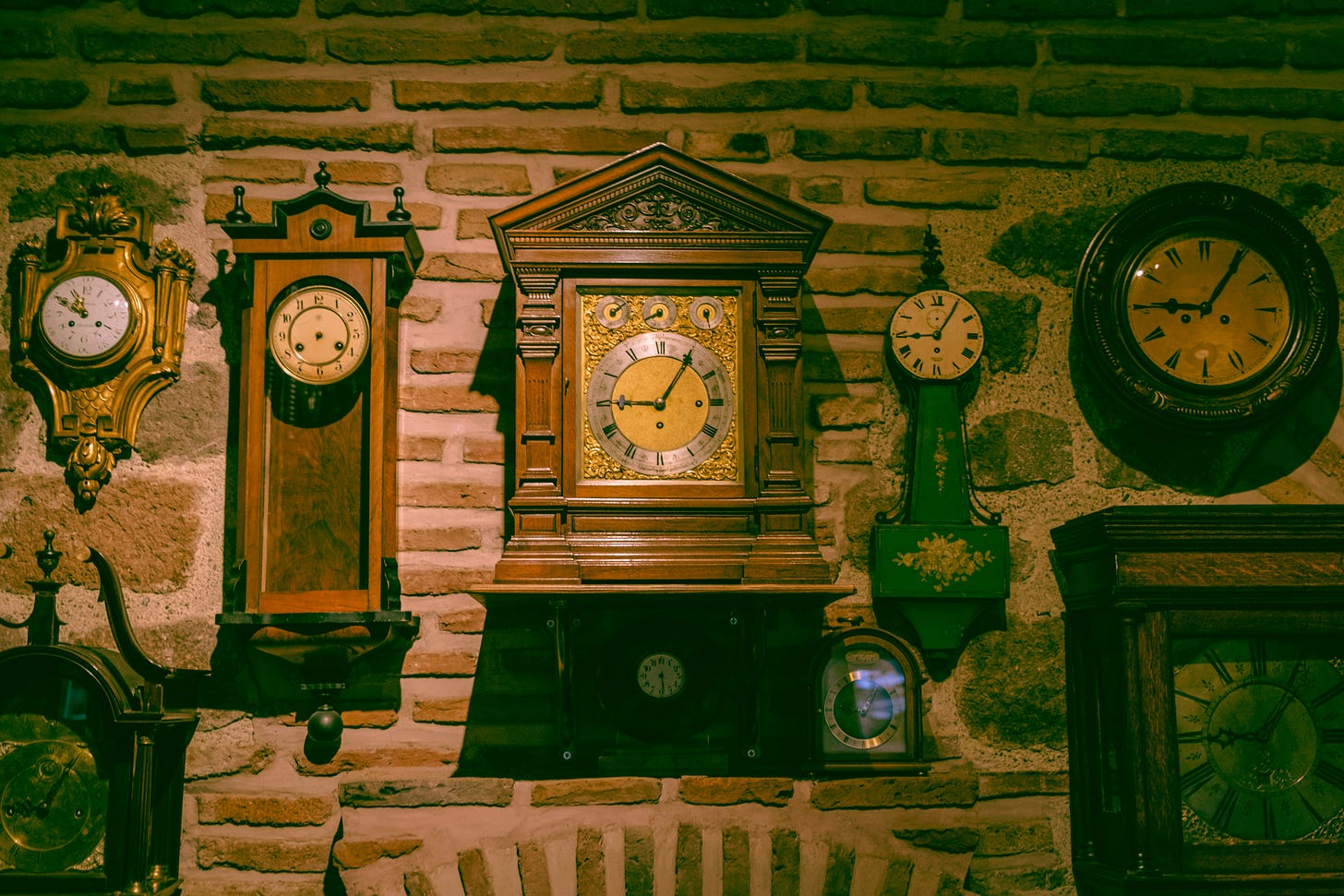A brick wall covered in ornate wooden and metal clocks.