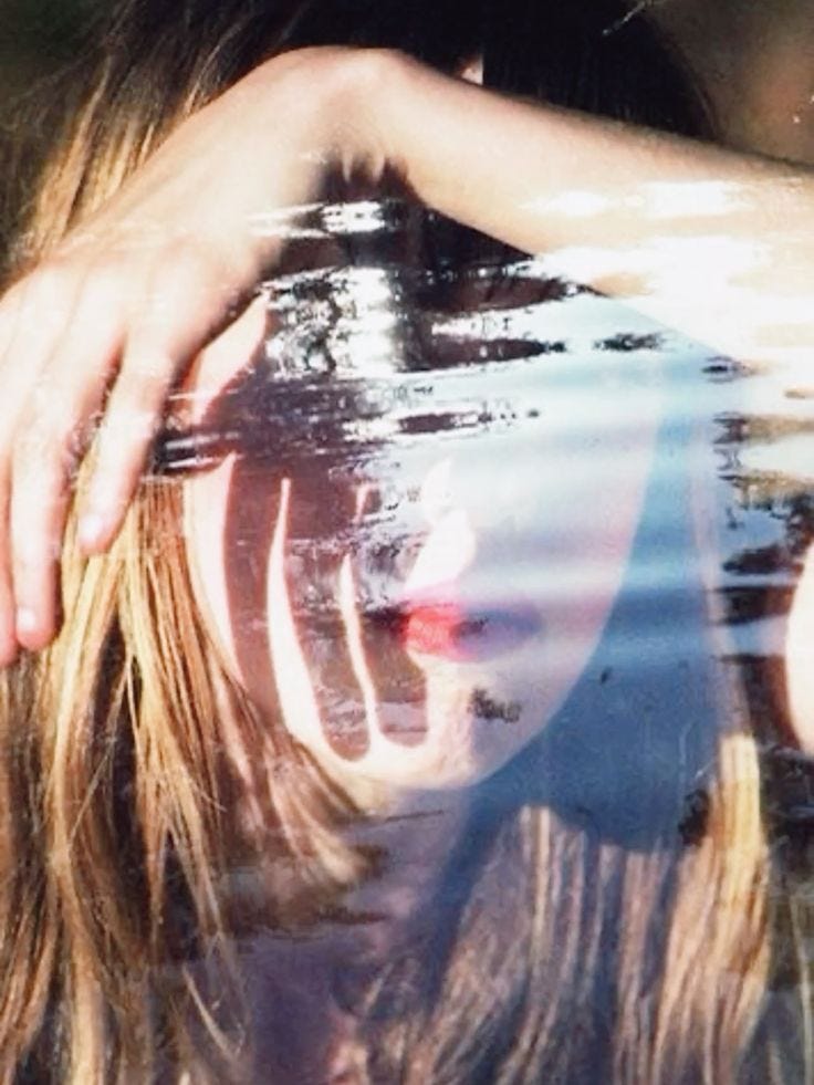 This may contain: a woman is reflected in the water with her hands on her head and hair blowing back