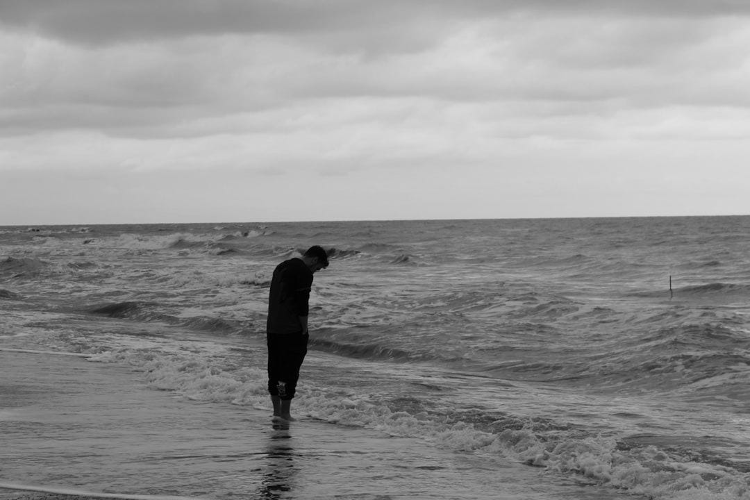 A person walks along a wet shore with choppy waves.