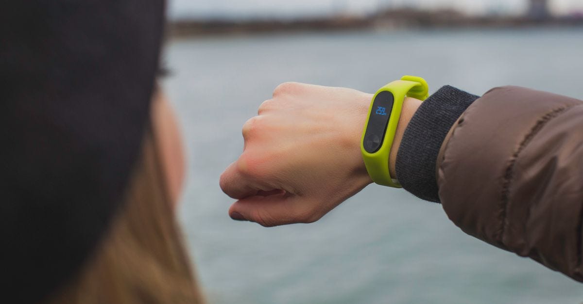Photo: Burst / Pexels Close-up of a woman outdoors checking the time on her smartwatch by a lake.
