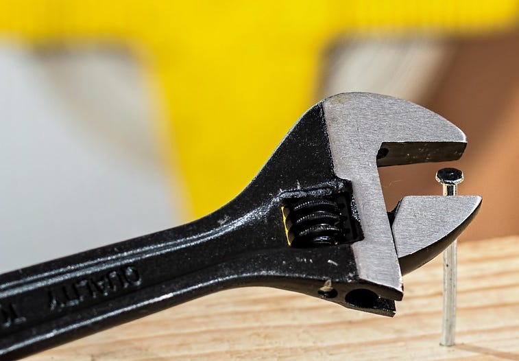 Photograph of a wrench about to be used on a nail.