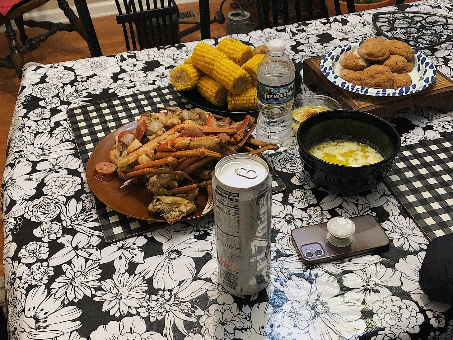 A dinner table with crab legs, a pile of corn on the cobs, a bowl of butter, water bottle, and a plate of ginger cookies