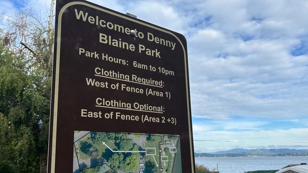A brown park sign reads "Welcome to Denny Blaine Park — Park Hours: 6am to 10pm — Clothing Required: West of Fence (Area 1) — Clothing Optional: East of Fence (Area 2+3)" with a small map inset at the bottom showing the zone divisions. Lake Washington and a partly cloudy sky are visible in the background.