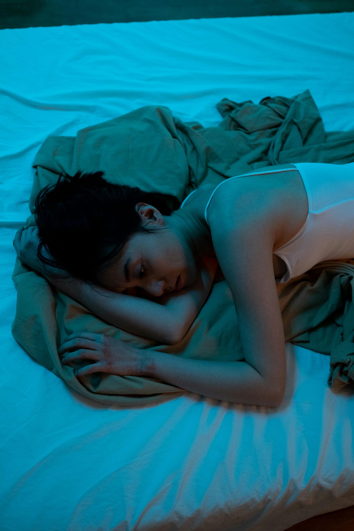 Free An adult woman lies on a bed in a dimly lit room, reflecting emotions of solitude and contemplation. Stock Photo