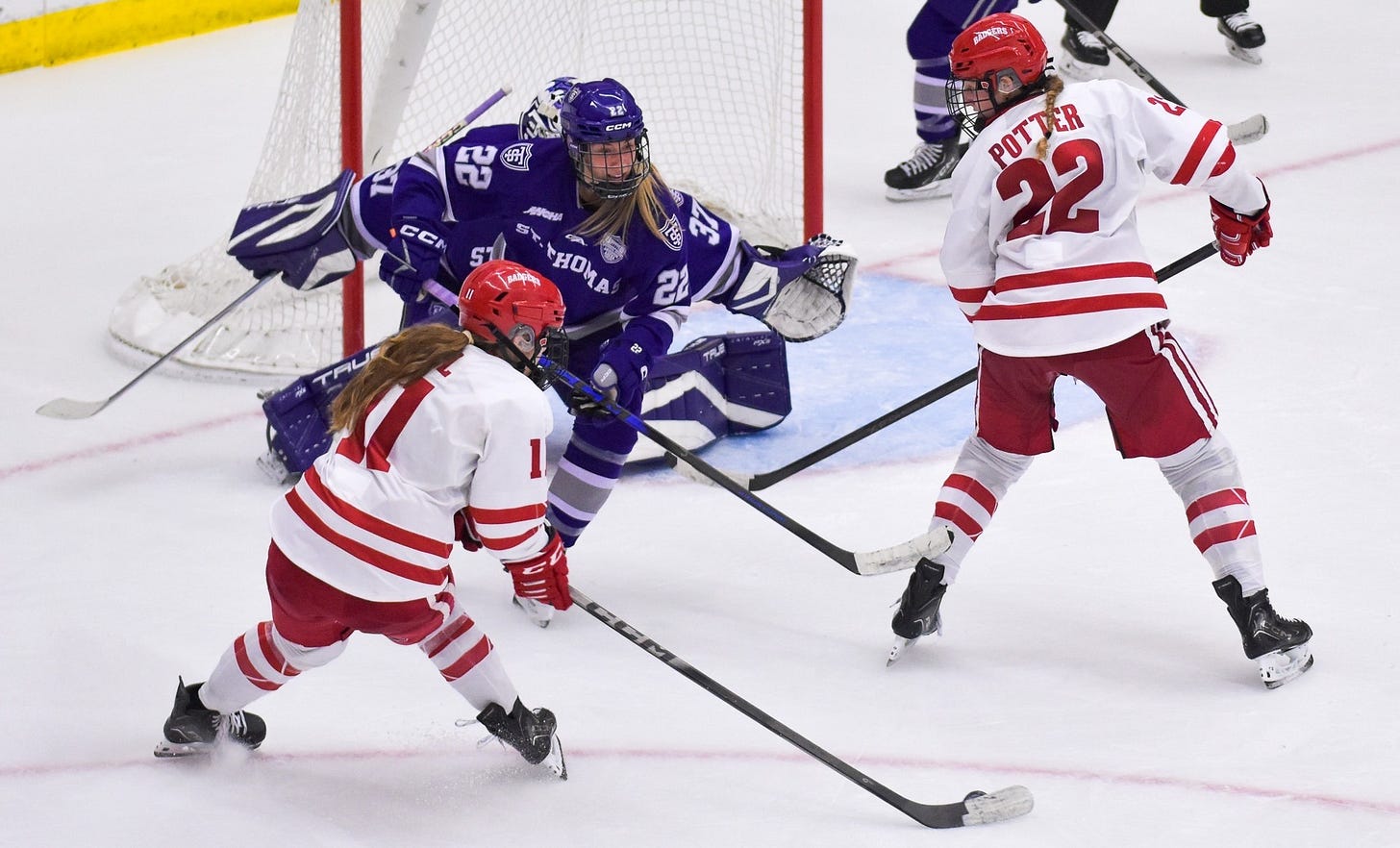 wisconsin women's hockey forward Cassie Hall with a puck on her stick shooting around a St. Thomas defender and Wisconsin's Laney Potter