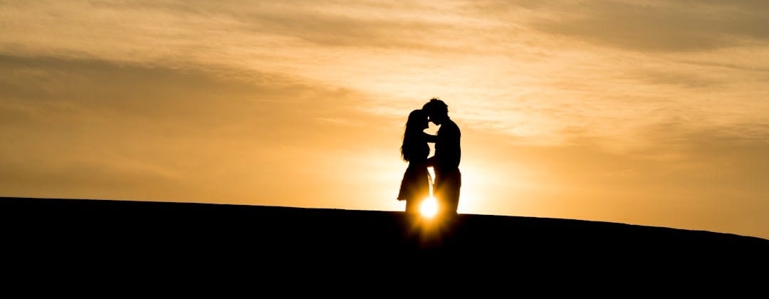man and woman's silhouette on hill during golden hour