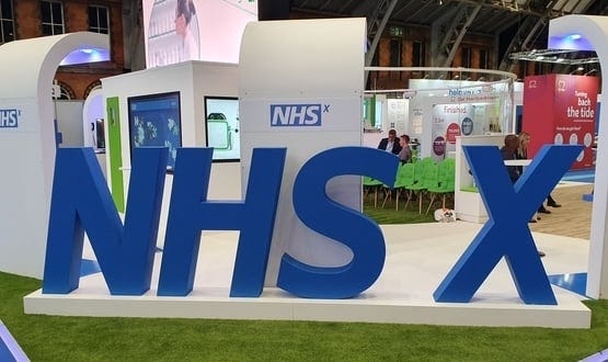 A photograph of a person-sized 3D model of the NHSX typographic logo.