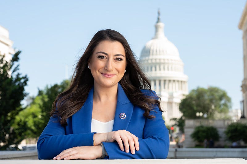 Professional portrait of Congresswoman Sara Jacobs smiling confidently in a blue blazer with congressional pin, arms crossed, standing outdoors with the U.S. Capitol building blurred in the background under a clear blue sky. Image for article on Sara Jacobs egg freezing journey, radical vulnerability, and women's agency in leadership. Professional portrait of Congresswoman Sara Jacobs smiling confidently in a blue blazer with congressional pin, arms crossed, standing outdoors with the U.S. Capitol building blurred in the background under a clear blue sky. Image for article on Sara Jacobs egg freezing journey, radical vulnerability, and women's agency in leadership.