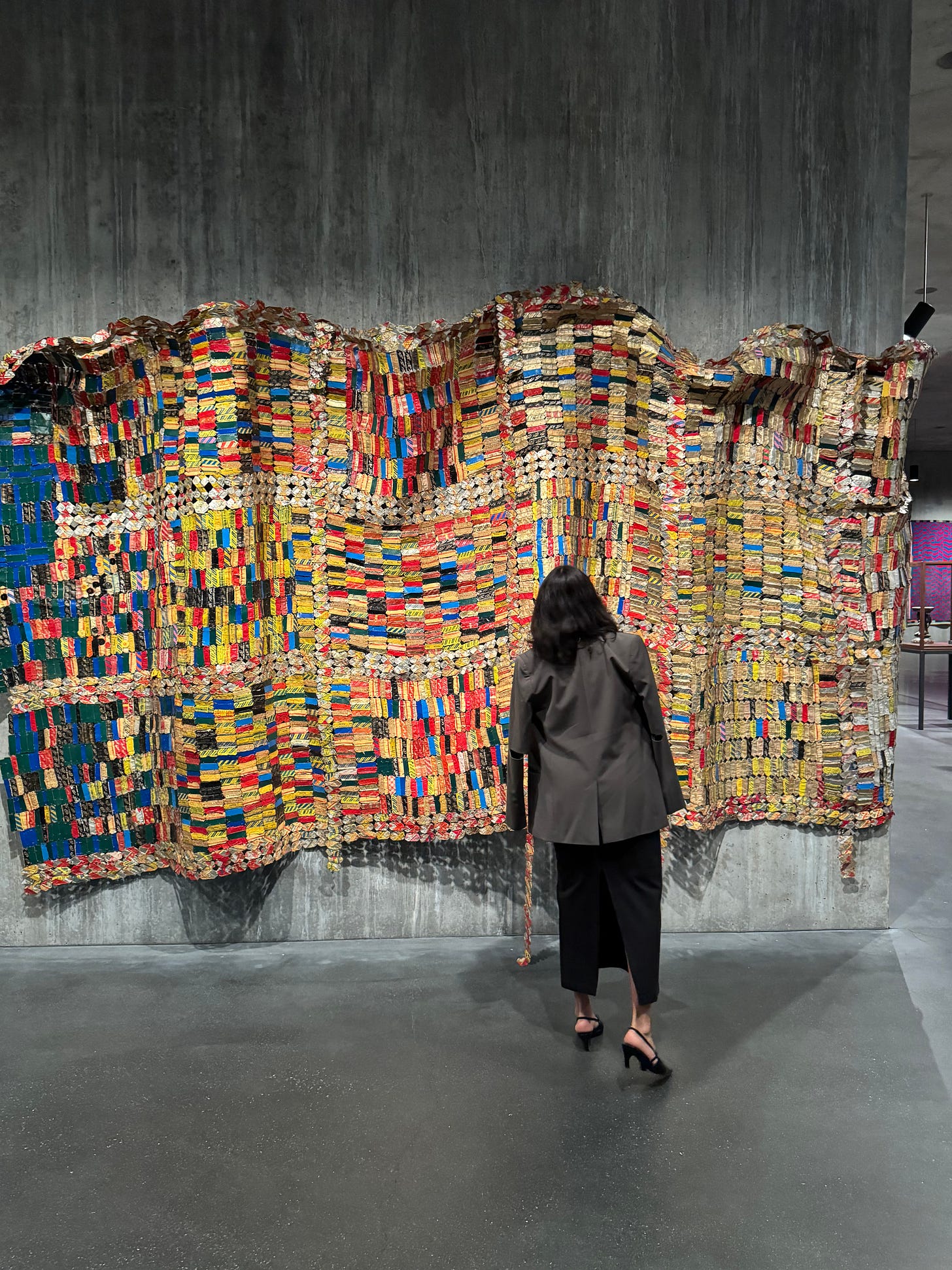 A visitor faces El Anatsui’s monumental rippling wall sculpture made from thousands of brightly colored metal bottle caps at LACMA.
