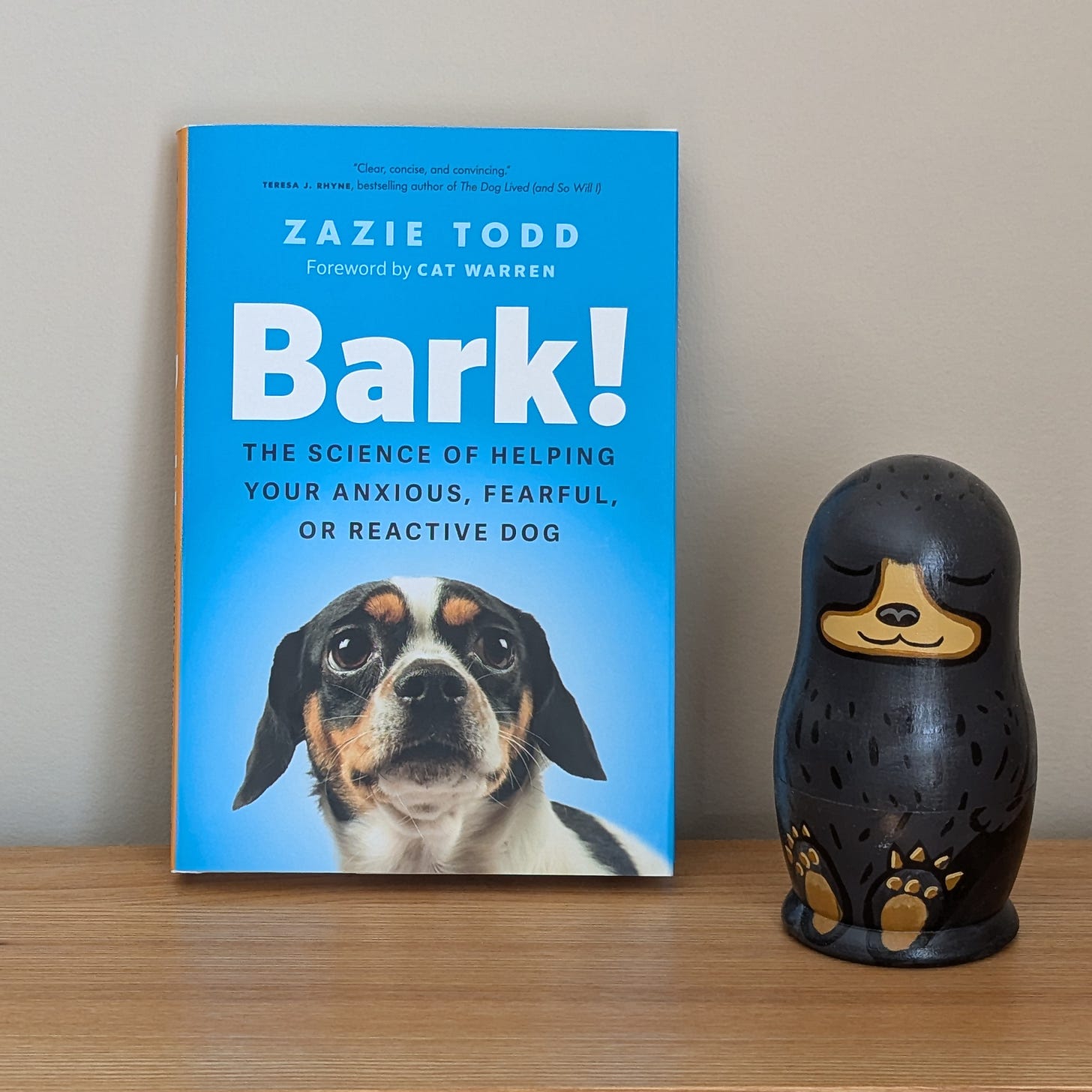 A copy of Bark! on a bookshelf next to a wooden bear. The cover of the book is blue with a cute Chihuahua