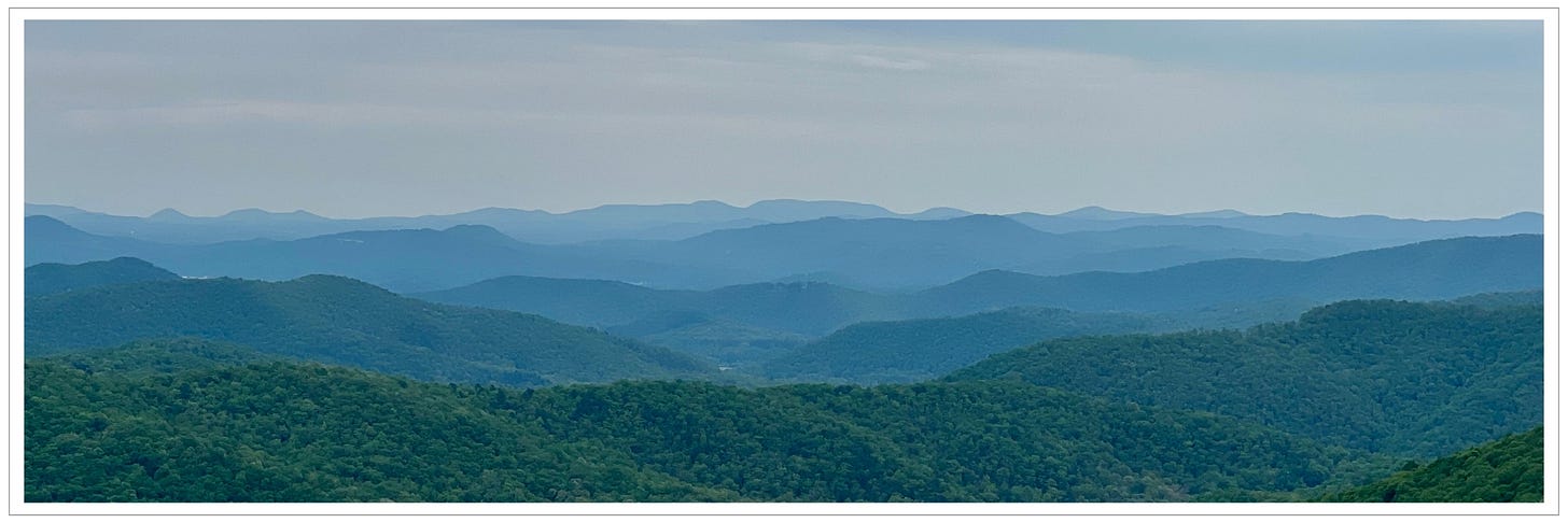 soft mists of clouds softening the ridges of layers of greening mountain ranges; mountain ridges blue in the distance fading into sky