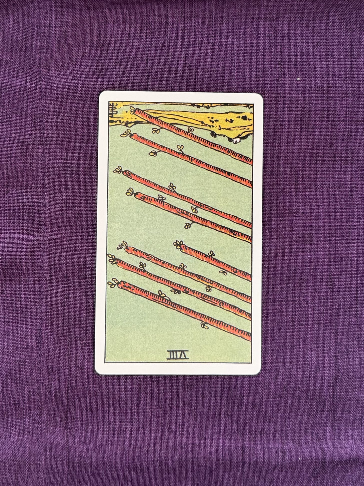 Eight wooden wands are shown suspended diagonally across the image, all angled in the same direction. They appear above an open landscape containing a river, green fields, and a small group of buildings in the distance. The sky is clear and occupies most of the background. No people or animals are present. Eight wooden wands are shown suspended diagonally across the image, all angled in the same direction. They appear above an open landscape containing a river, green fields, and a small group of buildings in the distance. The sky is clear and occupies most of the background. No people or animals are present.