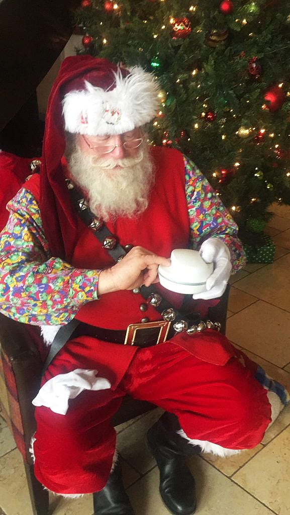 Santa sitting next to a decorated Christmas tree using a ClipDifferent Pro to trim his nails.