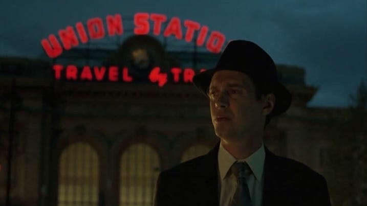 Union Station: Steve Buscemi’s character stands solemnly in front of Denver’s iconic Union Station at night, the neon red letters glowing behind him.