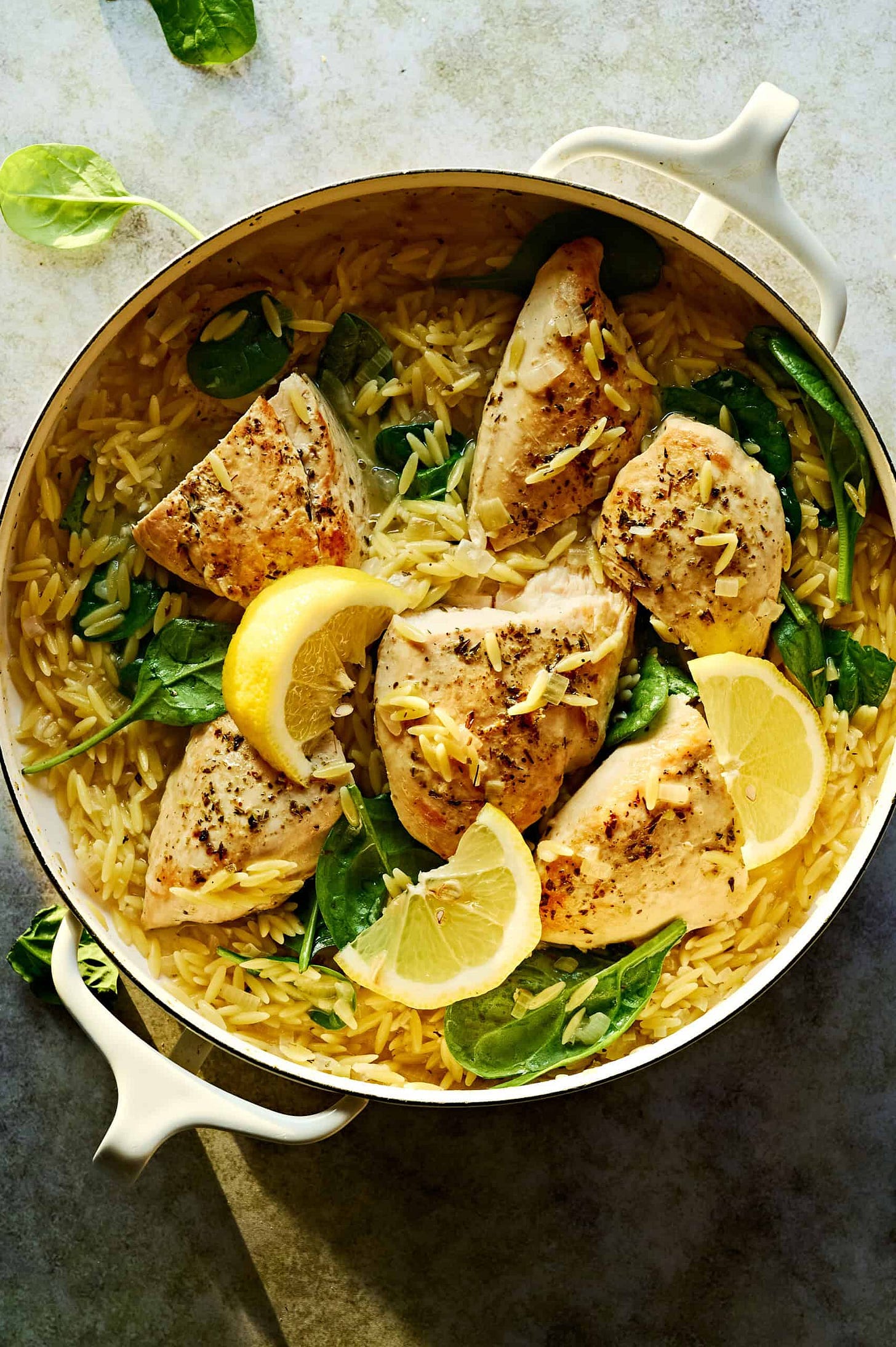 Lemon chicken orzo pasta bright and gorgeous with sliced lemon wedges, and garnished with fresh spinach leaves.