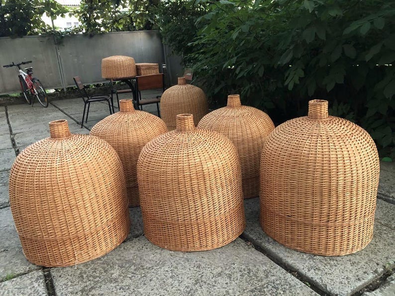 May include: A collection of woven rattan lampshades in various sizes. The lampshades have a rounded, bell-like shape with a cylindrical neck. The natural tan color of the rattan creates a warm, inviting aesthetic. The lampshades are suitable for indoor or outdoor use. May include: A collection of woven rattan lampshades in various sizes. The lampshades have a rounded, bell-like shape with a cylindrical neck. The natural tan color of the rattan creates a warm, inviting aesthetic. The lampshades are suitable for indoor or outdoor use.