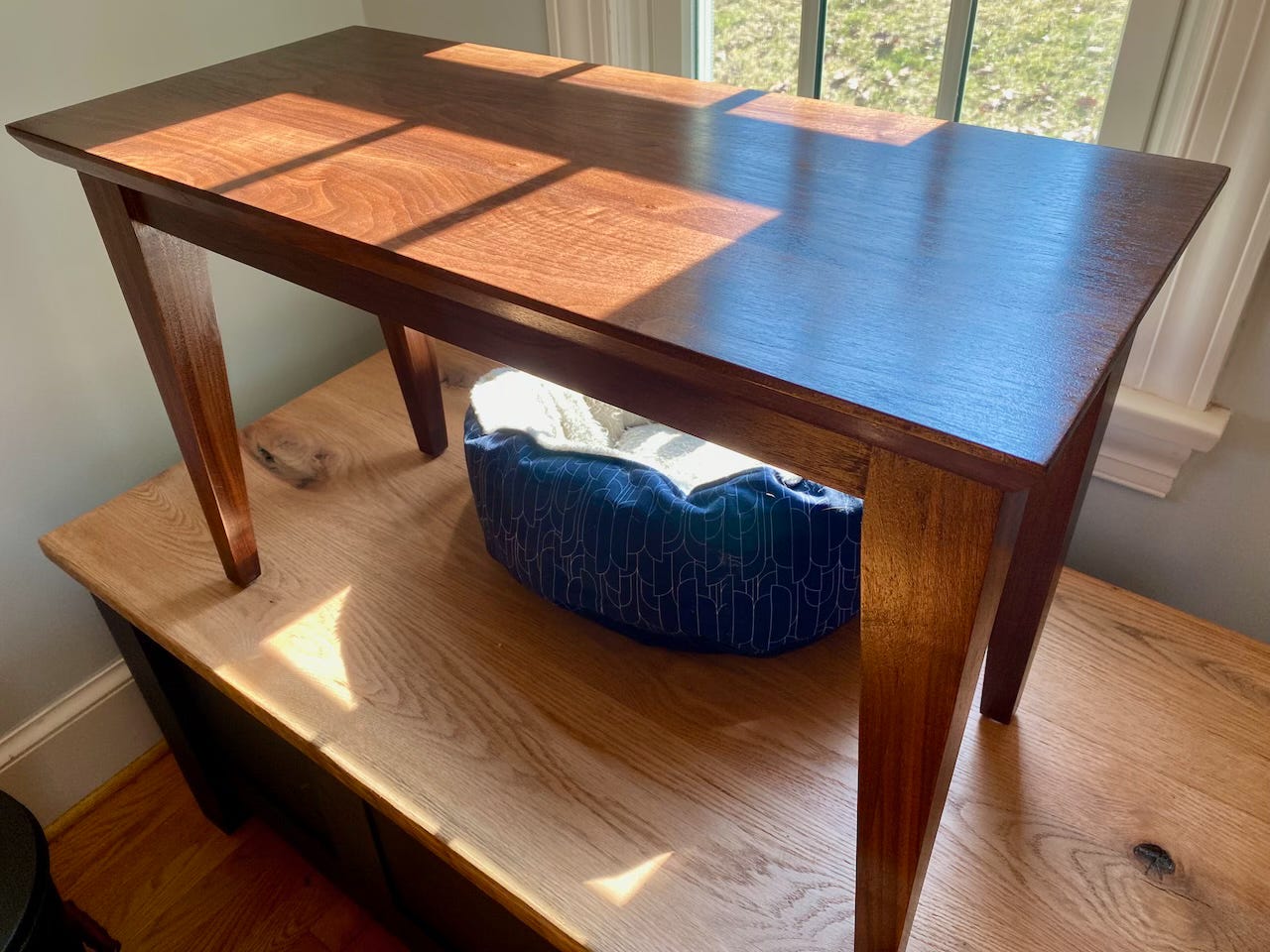 A walnut piano bench sitting under a window.