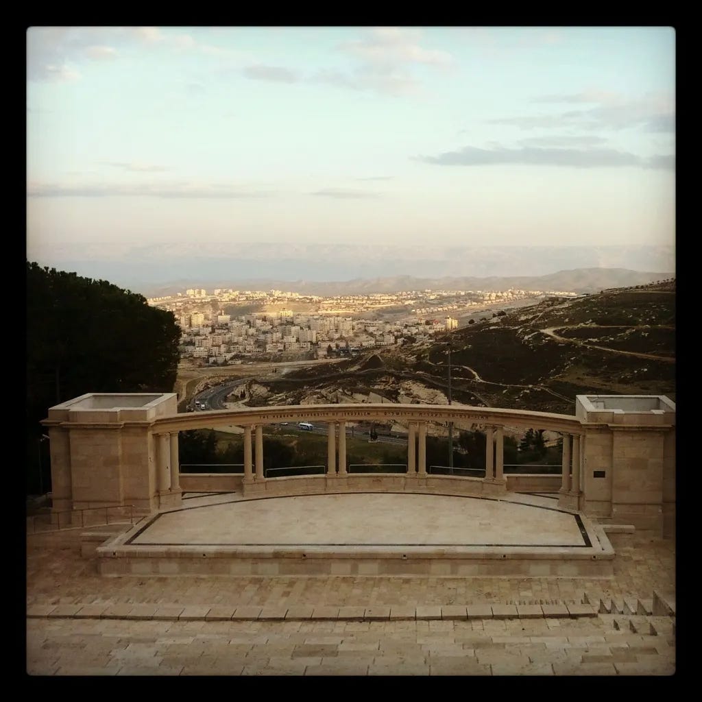 A stone stairs with a railing and a city in the background

Description automatically generated