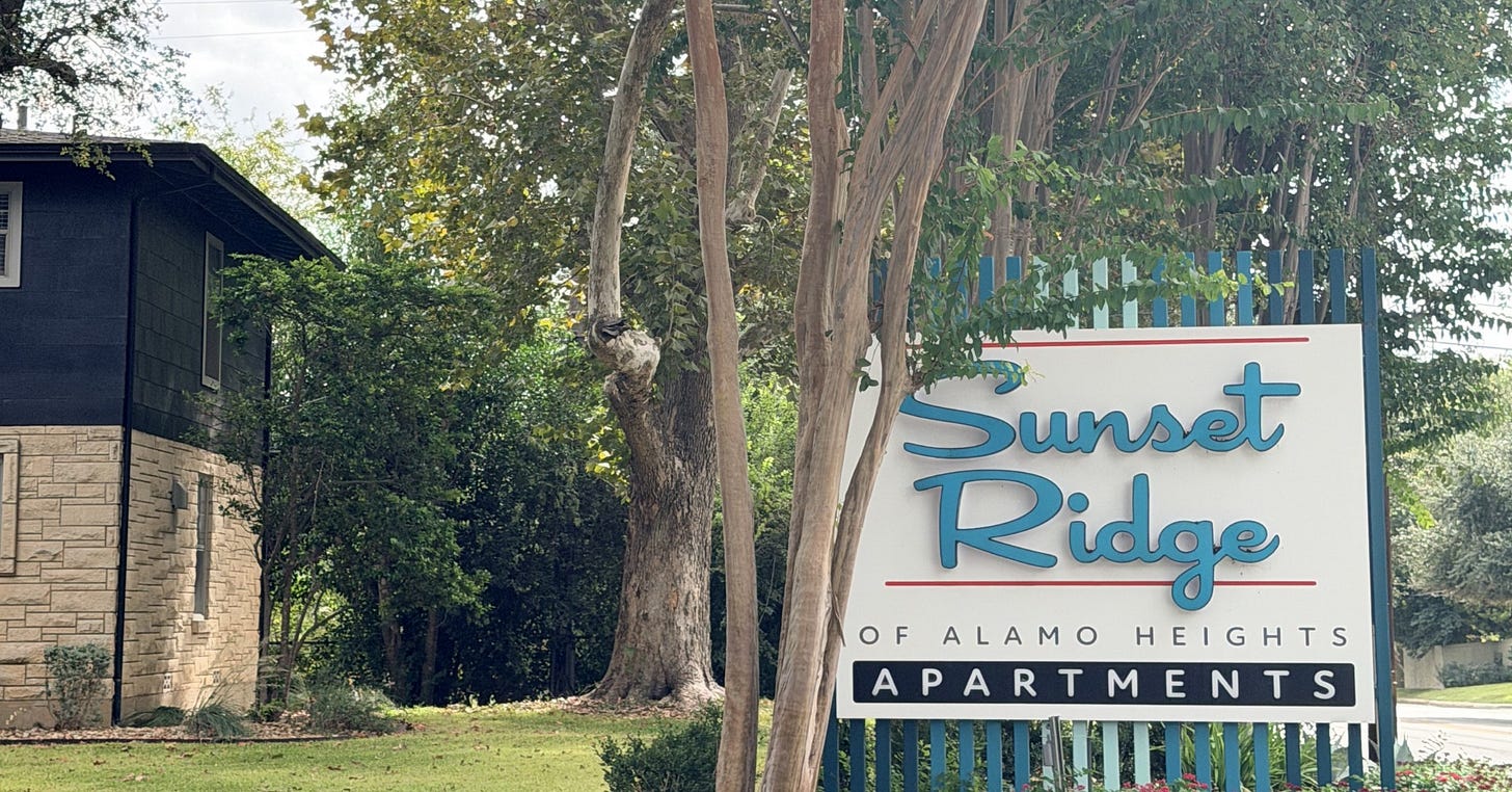 The Sunset Ridge of Alamo Heights apartments sign beside one of the complex's original two-story buildings in Terrell Heights