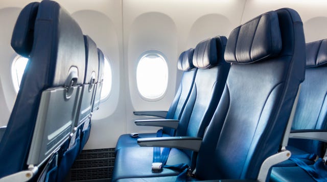 Empty row of airplane seats with window and aisle visible on a morning flight.