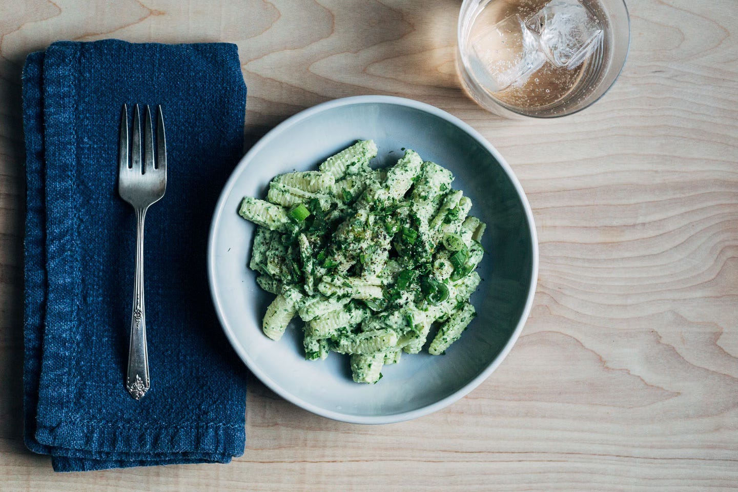 A bowl of pasta with feta sauce, with a napkin, fork, and glass of water alongside. 