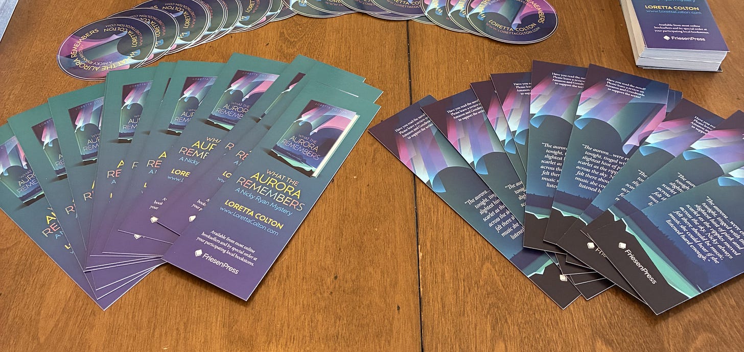 Photo of several bookmarks and round stickers advertising "What the Aurora Remembers", fanned out messily on a table