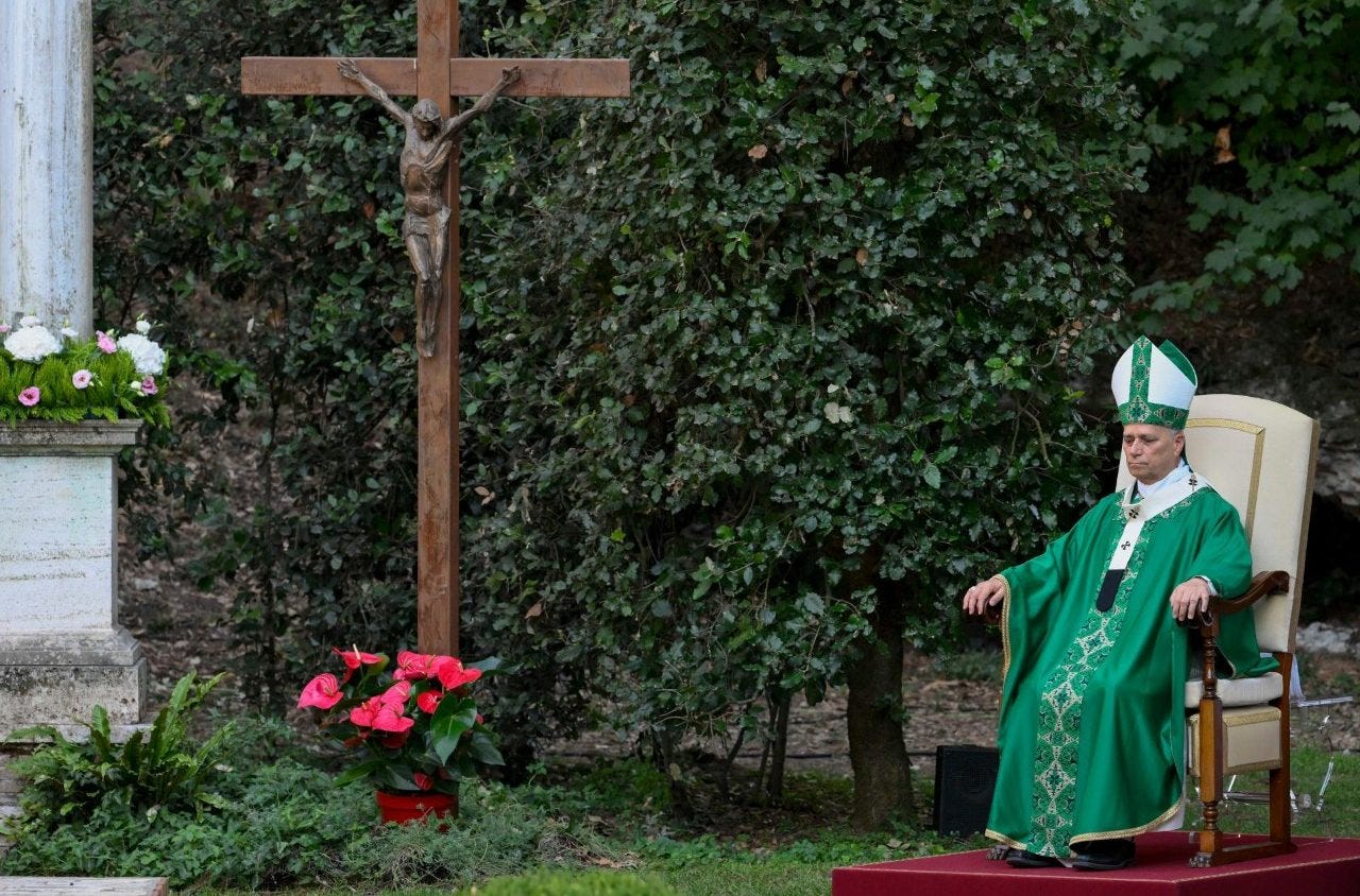 Pope Leo XIV in green vestments seated in the garden of the Borgo Laudato Si’ at Castel Gandolfo, a crucifix among the trees beside him Pope Leo XIV in green vestments seated in the garden of the Borgo Laudato Si’ at Castel Gandolfo, a crucifix among the trees beside him