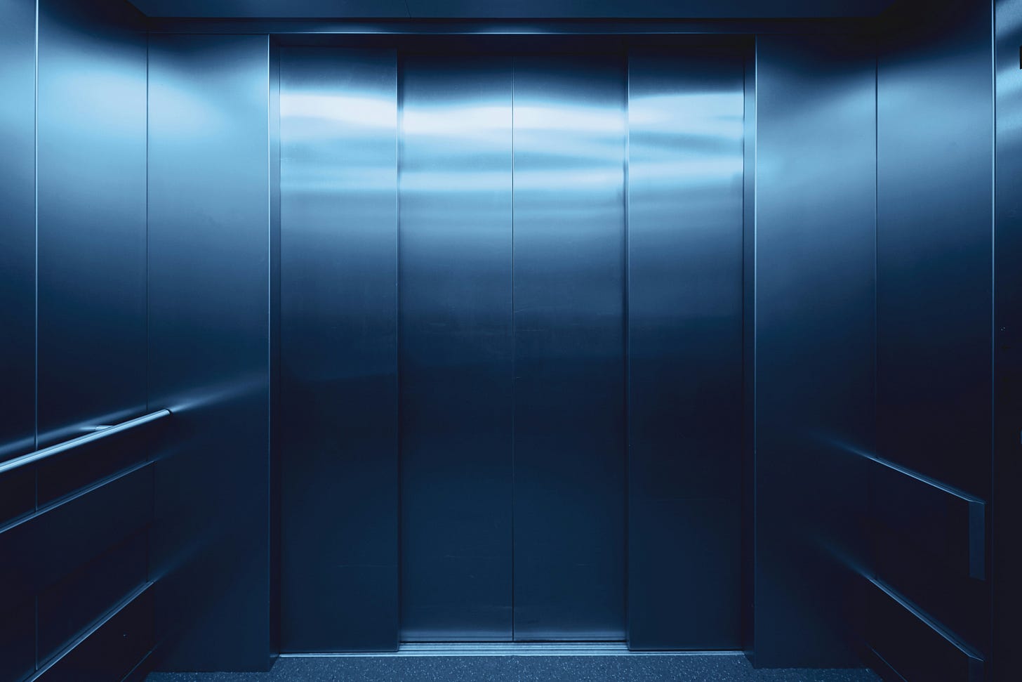 The inside of an elevator. The doors and walls are silver. 