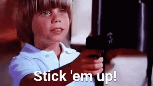 a young boy is pointing a gun at the camera and saying `` stick 'em up '' .