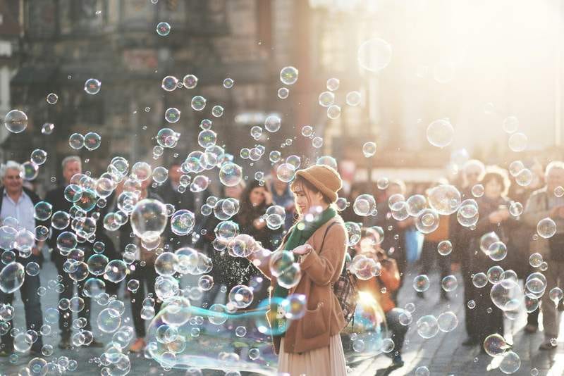 Unsplash photo of a woman surrounded by soap bubbles in a sunlit city square.