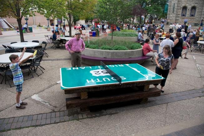 Another view of people playing ping-pong on a table made from a recycled highway sign.