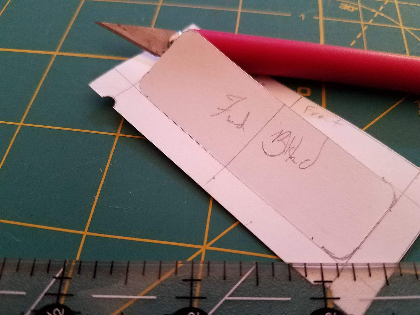 A closeup of a paper cutout piece and xacto knife. The paper reads “Fwd Blkhd”