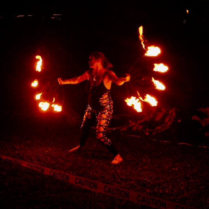 Two low-light photos of a fire performer spinning flaming props during MoonGroove's Saturday night show, trails of fire glowing orange and red against the dark sky.
